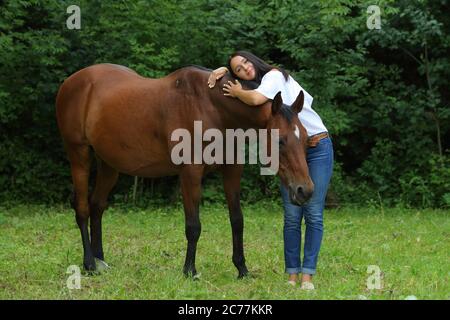 Hübsches Mädchen lächelt streichelt glatt das Pferd`s Mähne auf dem Feld. Zaum, Erwachsener. Stockfoto